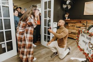 A romantic proposal moment captured in a cozy indoor space with wooden walls and French doors.