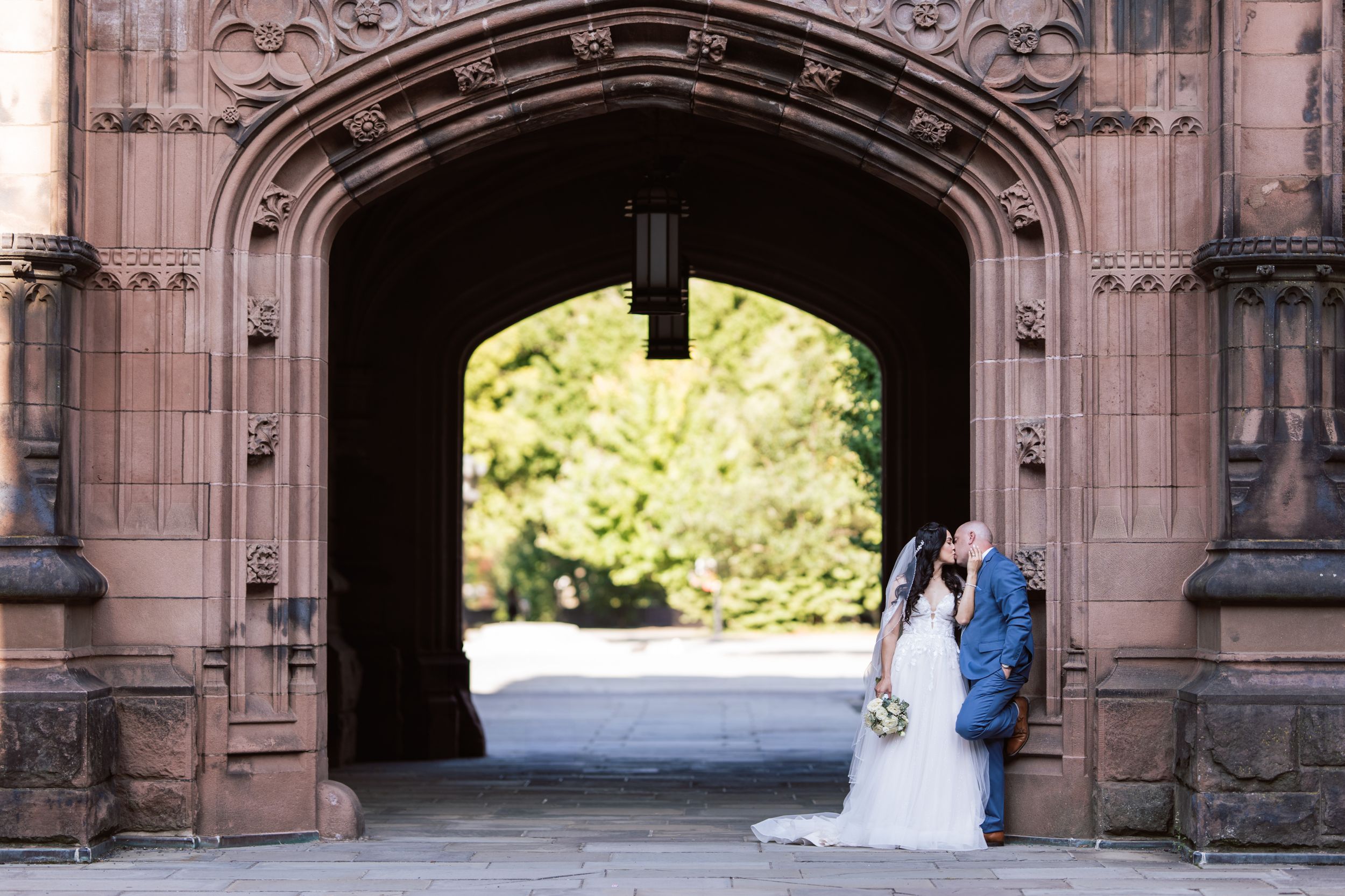 A couple stands in a ornate stone archway entrance during a wedding ceremony at a historic building.