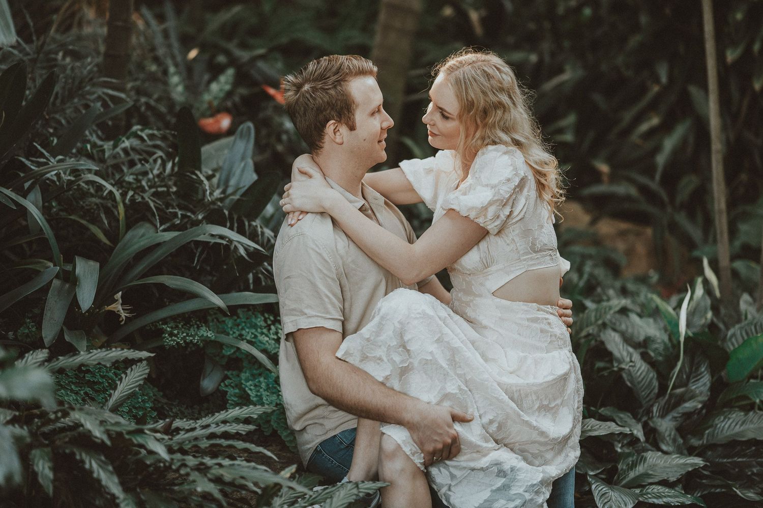 Romantic couple embracing outdoors among tropical foliage.