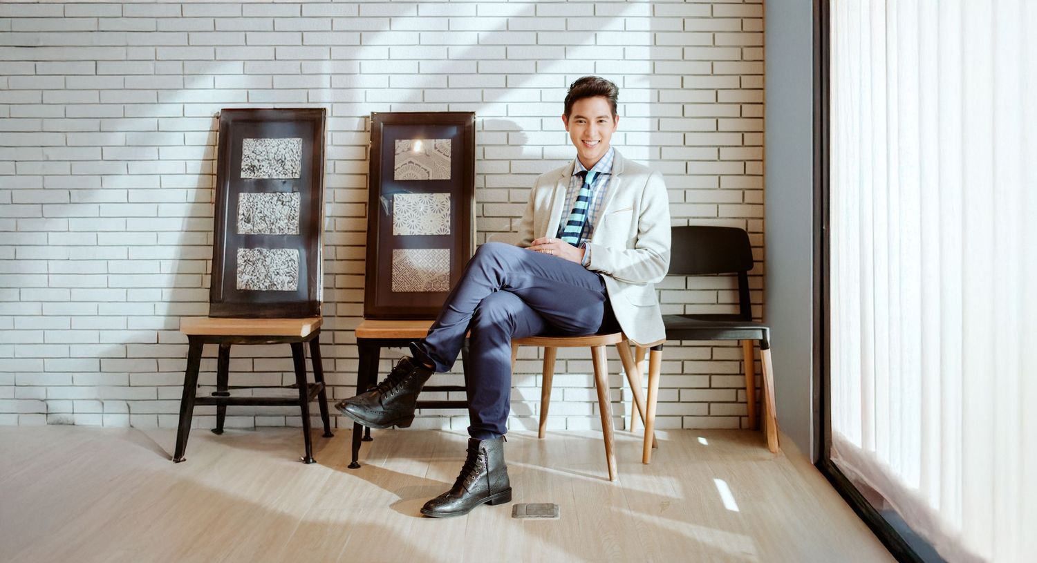 Professional seated in casual pose against brick wall with bookshelves in modern setting.