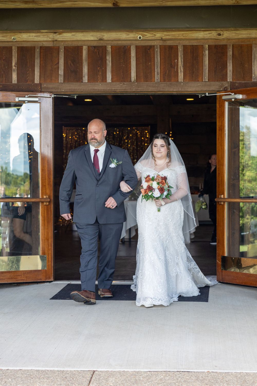 A wedding couple exits through wooden doors at a rustic venue entrance during their ceremony.