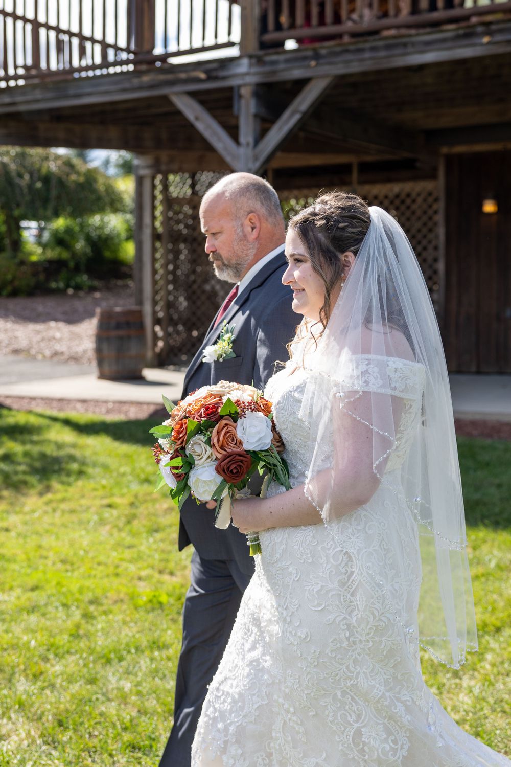 A wedding ceremony moment as a bride in a lace dress with veil holds a colorful bouquet in an outdoor garden setting.