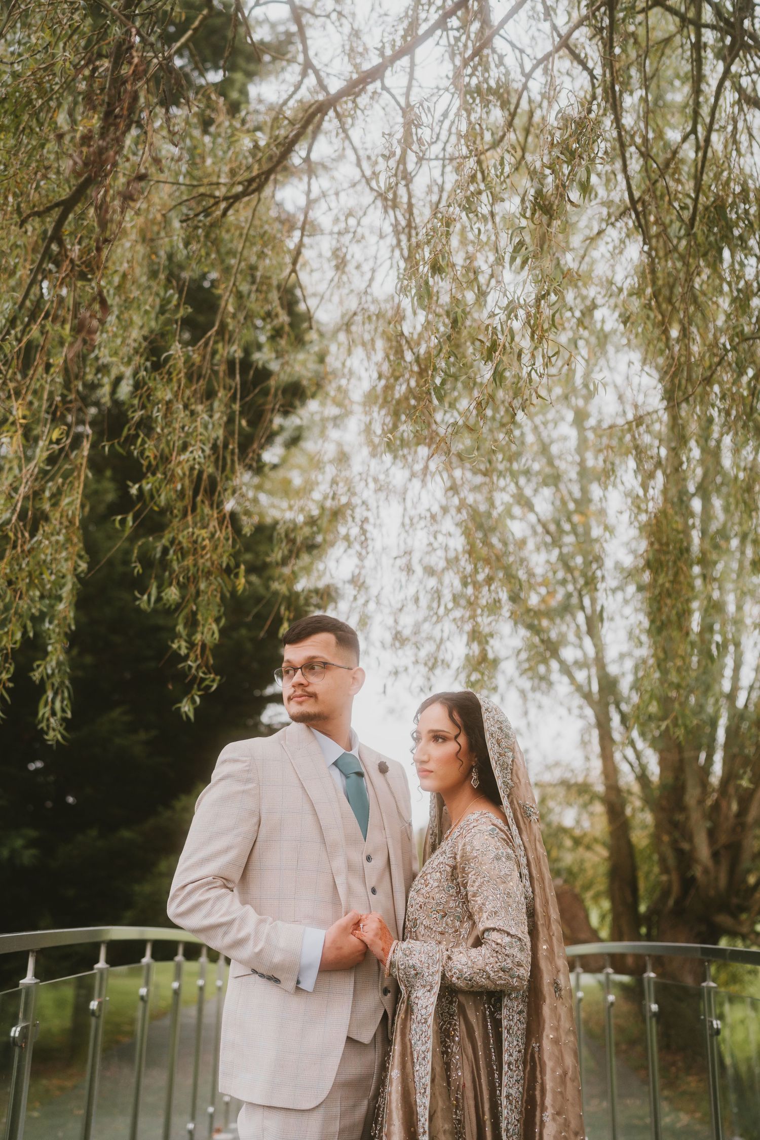 Elegant couple in formal attire posing against a backdrop of willow trees.