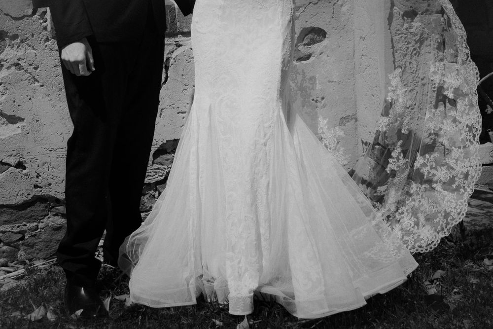 Close-up black and white photo of a flowing wedding dress and formal shoes.