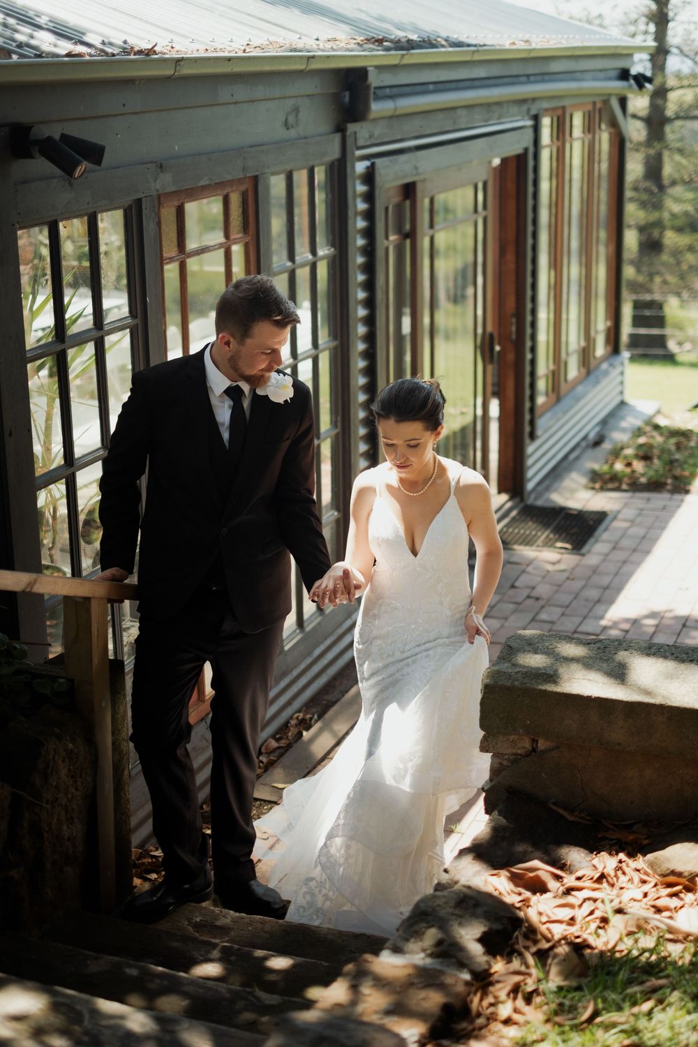 A couple exploring a rustic greenhouse structure filled with dappled sunlight.
