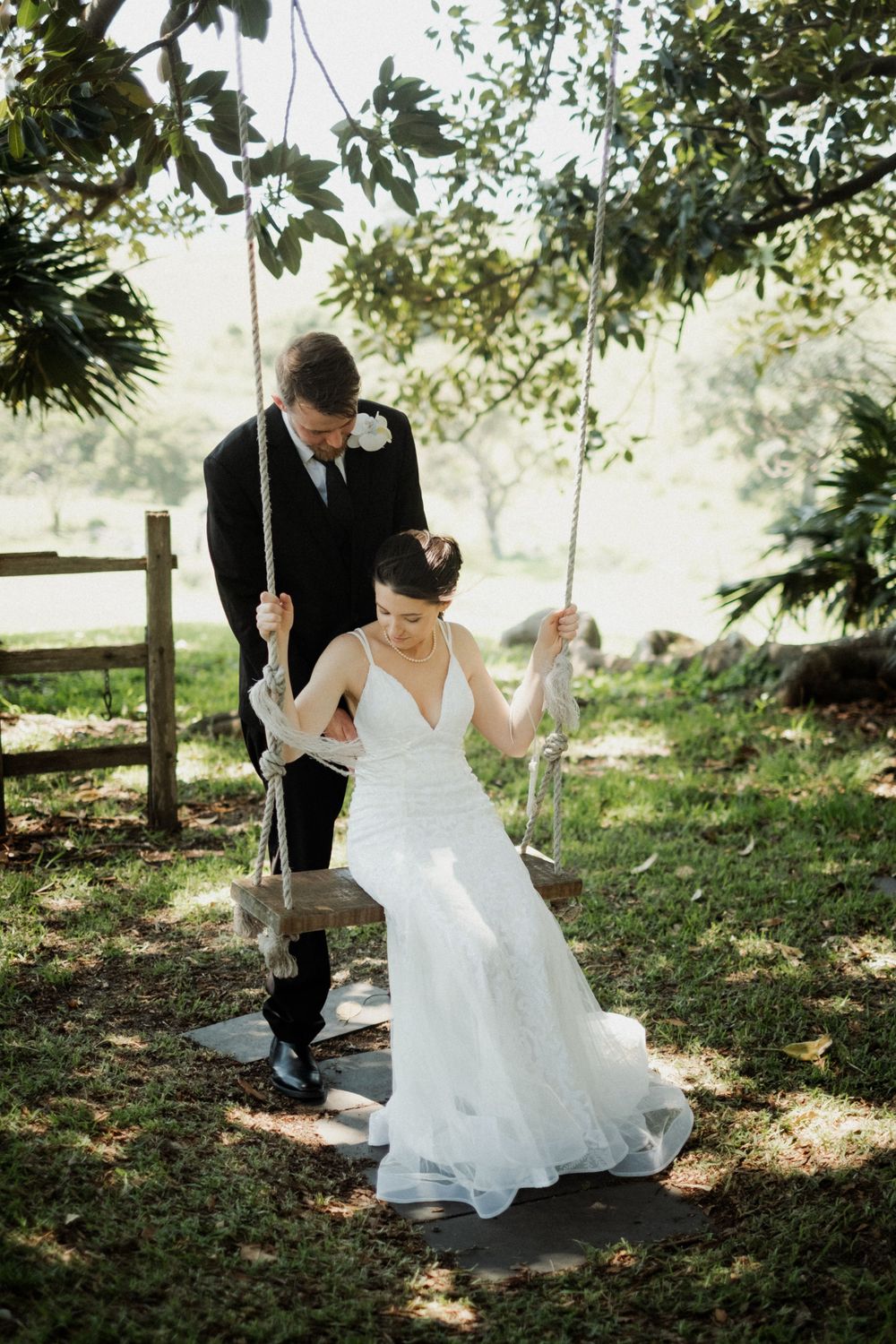 A couple enjoying playful moments on tree swings in a sunlit garden setting.