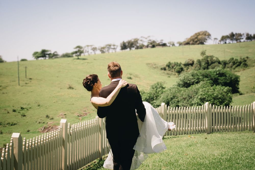 Wedding couple walking along a picket fence on a grassy hillside.