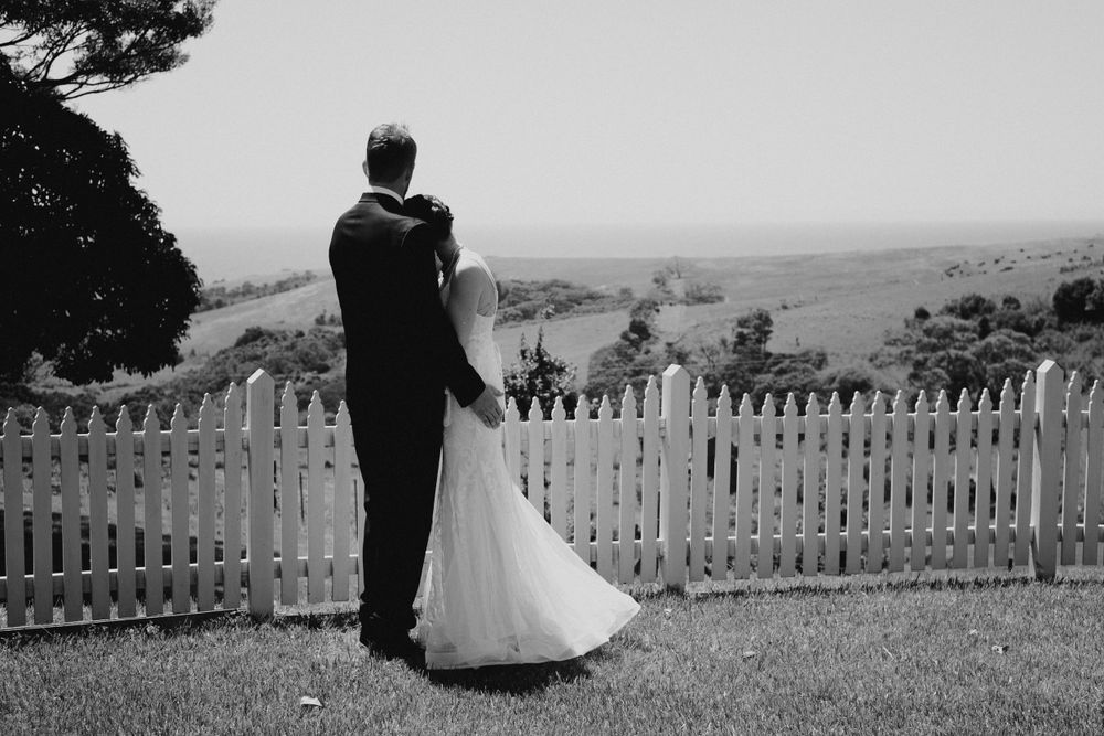 Black and white panoramic view of a couple by a white picket fence on a hilltop.
