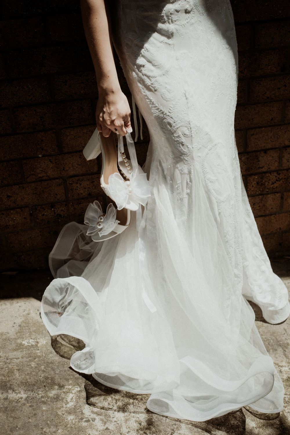 Close-up shot of a white wedding dress hem and bride's shoes on stone flooring.