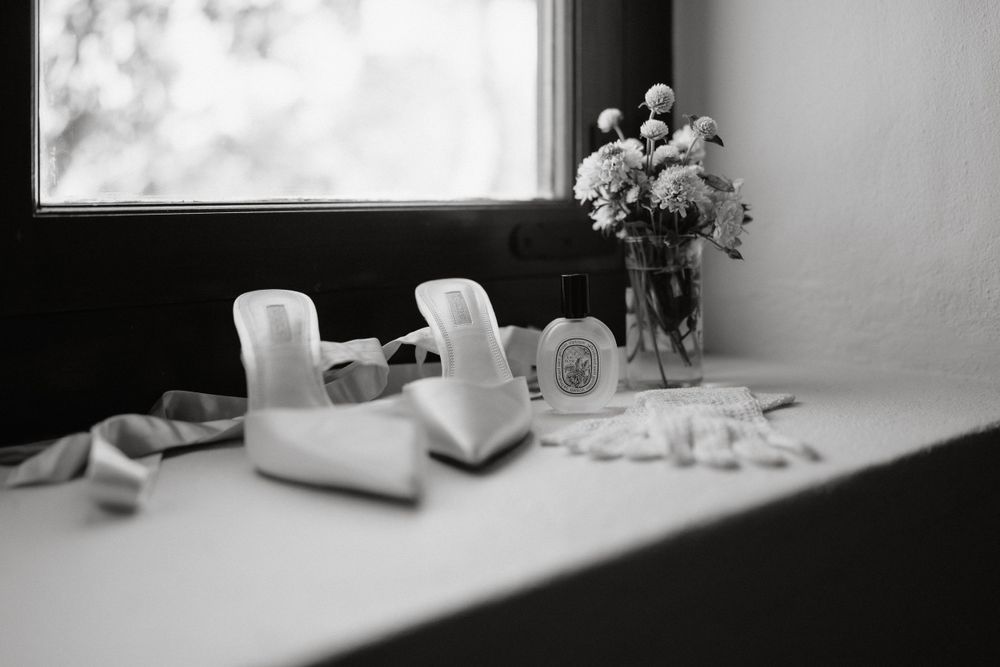 Black and white photo of high heels and floral arrangement by a window.