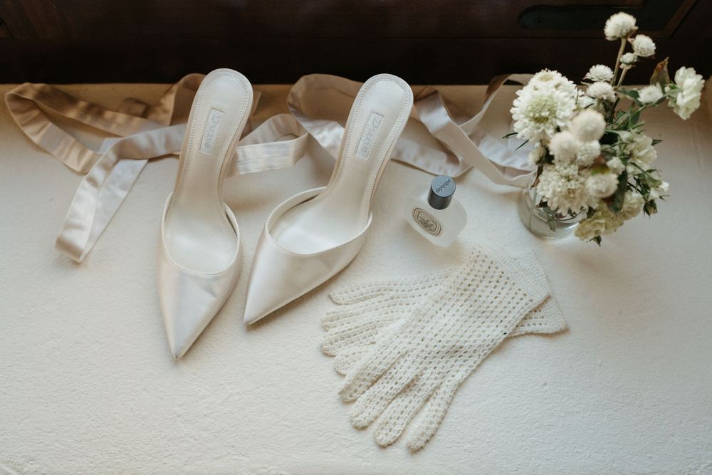 Elegant white wedding shoes and lace gloves arranged with delicate baby's breath flowers on light surface.