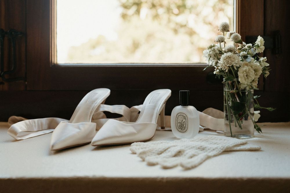 Wedding accessories including white heels, gloves and floral arrangement displayed on table.