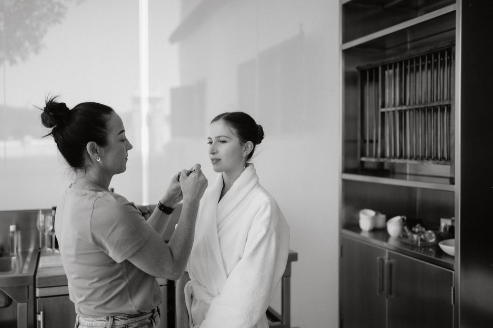 A makeup artist applying cosmetics to someone in a white robe.