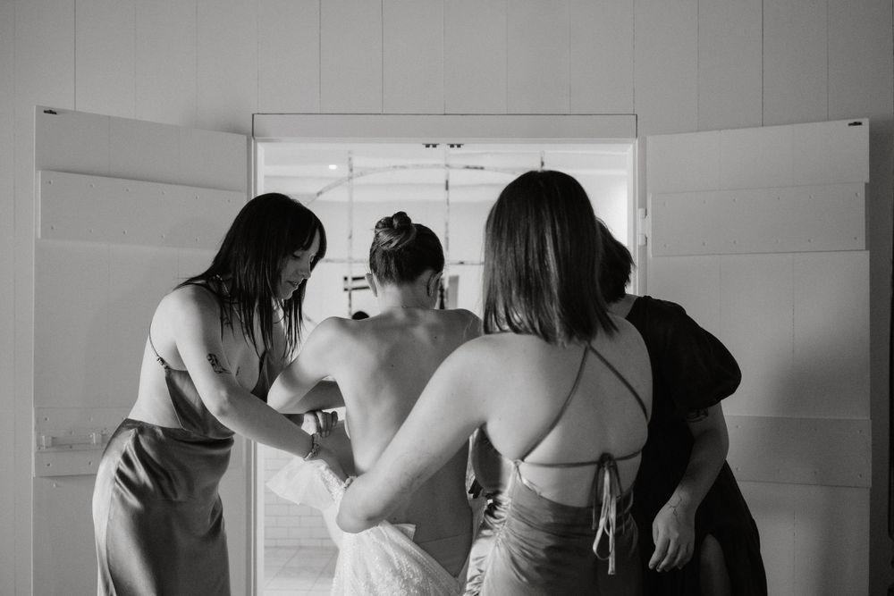 Black and white photo of bridesmaids helping with wedding dress preparations.