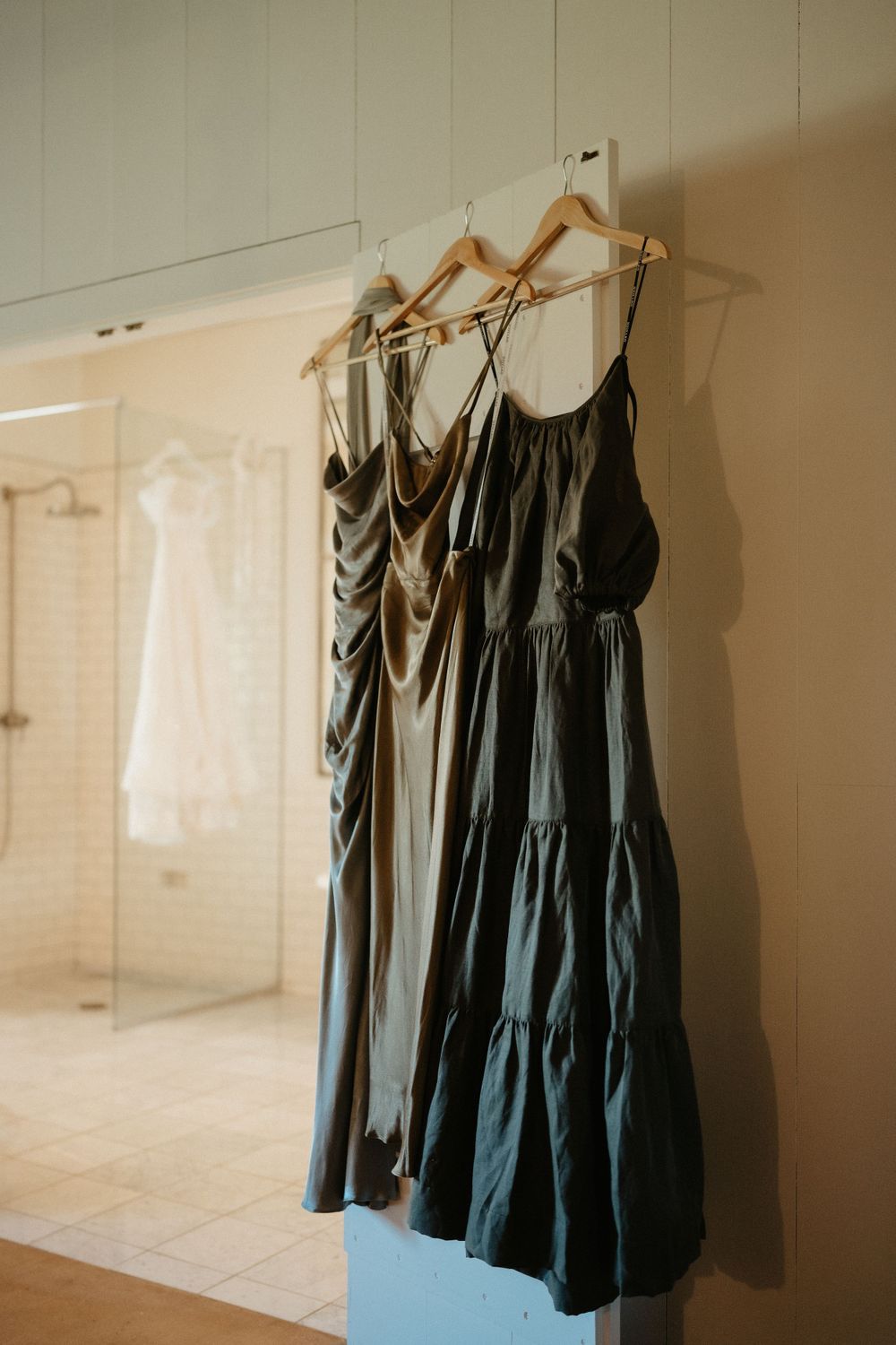 Dark bridesmaid dresses hanging on wooden hangers against a light wall.