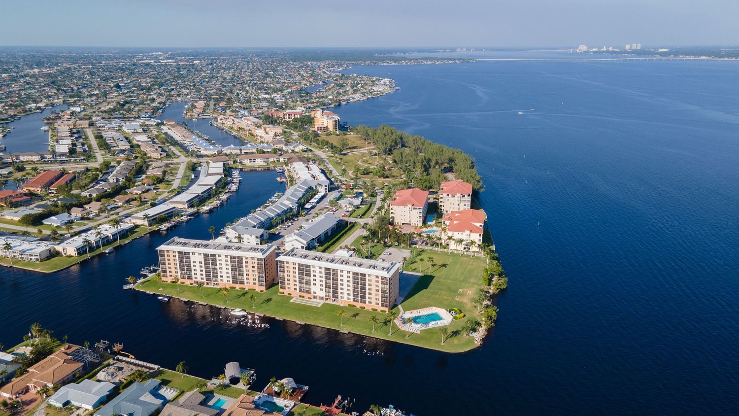 Aerial view of waterfront residential community with terracotta roofs and small lake in South Florida.