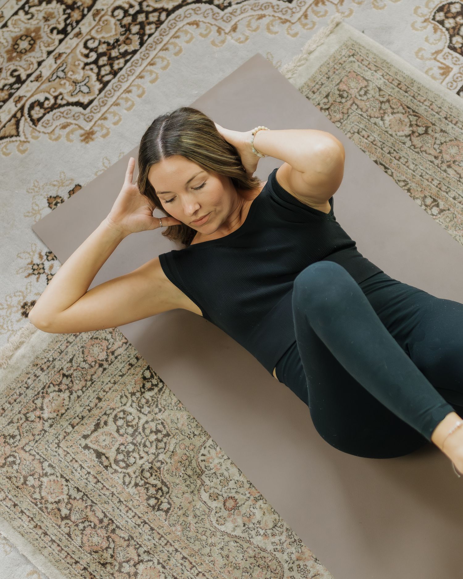 Person doing core exercises on yoga mat over ornate patterned rug.