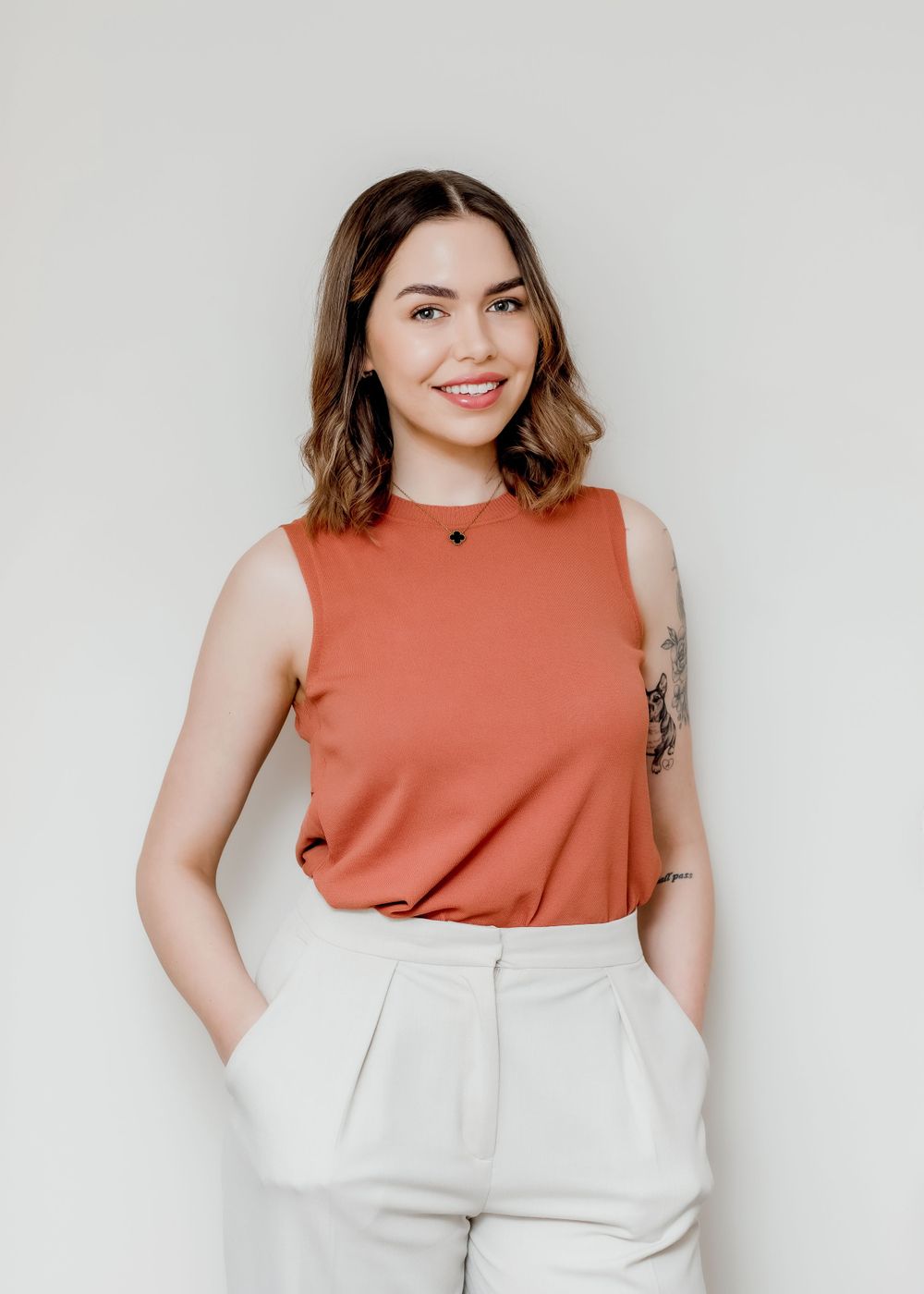 Professional wearing coral sleeveless top and white pants in minimalist studio setting.