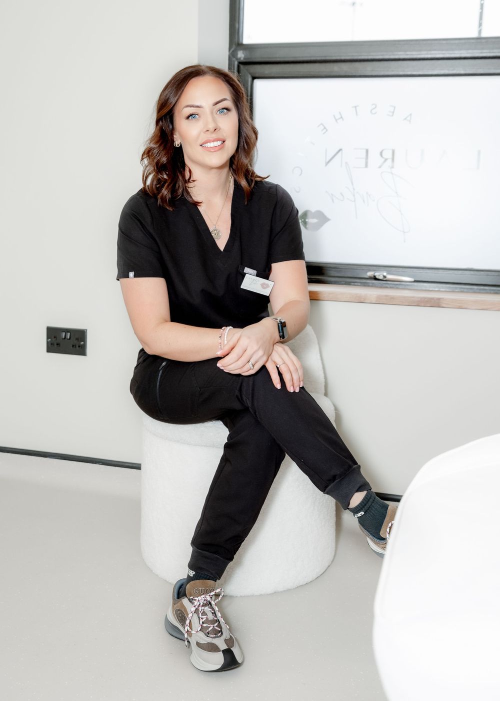 Medical professional in casual uniform sitting on white chair near workspace.