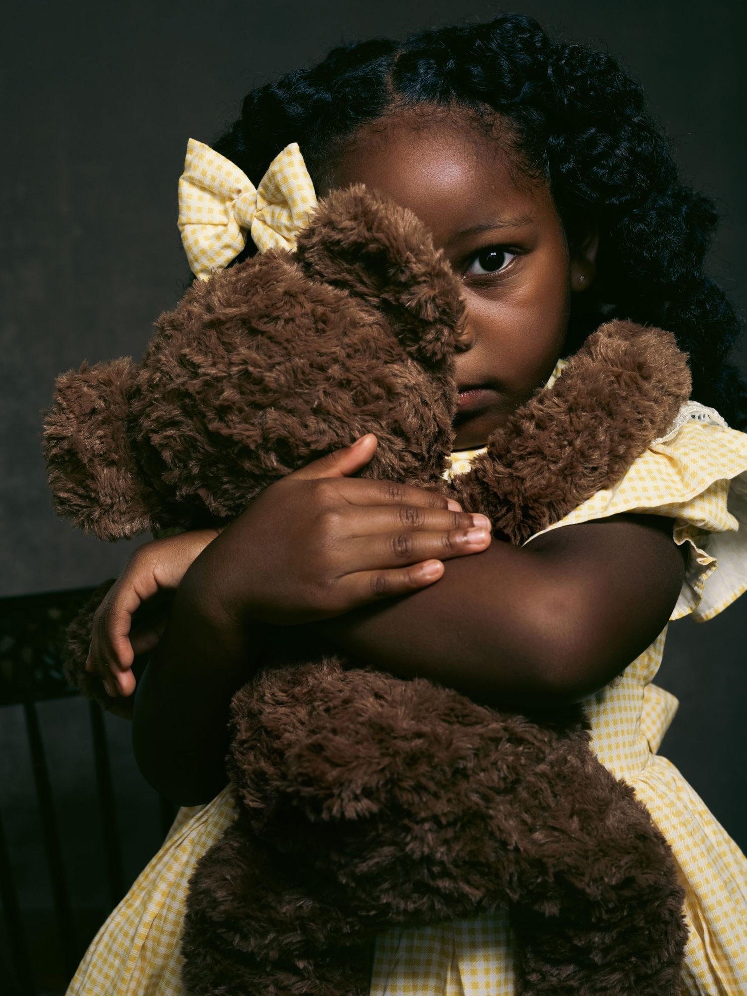 A series of artistic portrait photos showing someone in a yellow gingham dress holding a brown teddy bear against a dark background.