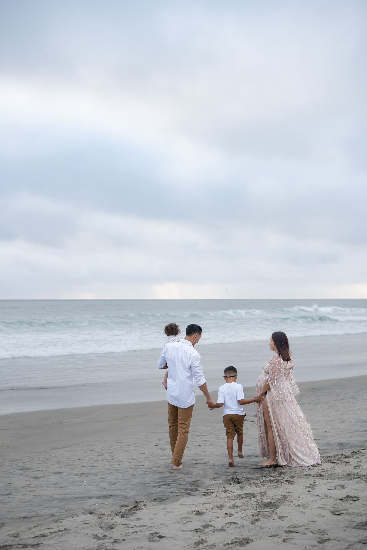Family walking together hand in hand along a cloudy beach at dusk.
