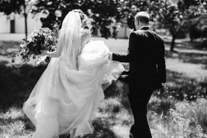 Black and white photo of newlyweds walking together as the bride's dress flows in the wind.