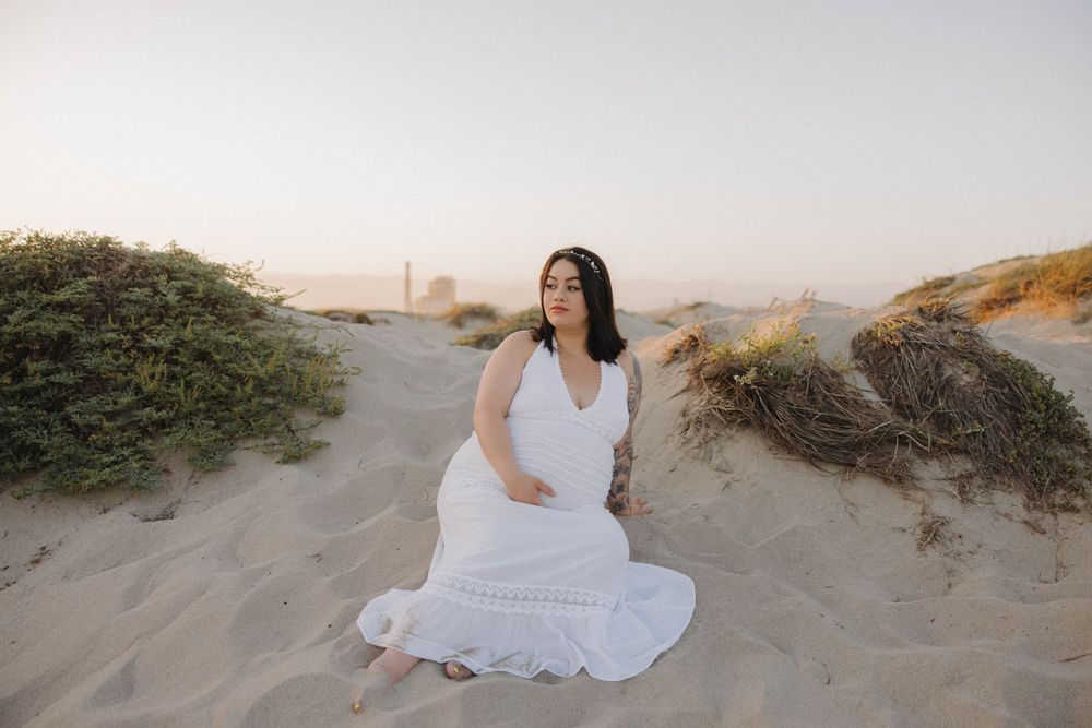 A white dress flows elegantly among sandy coastal dunes at sunset.