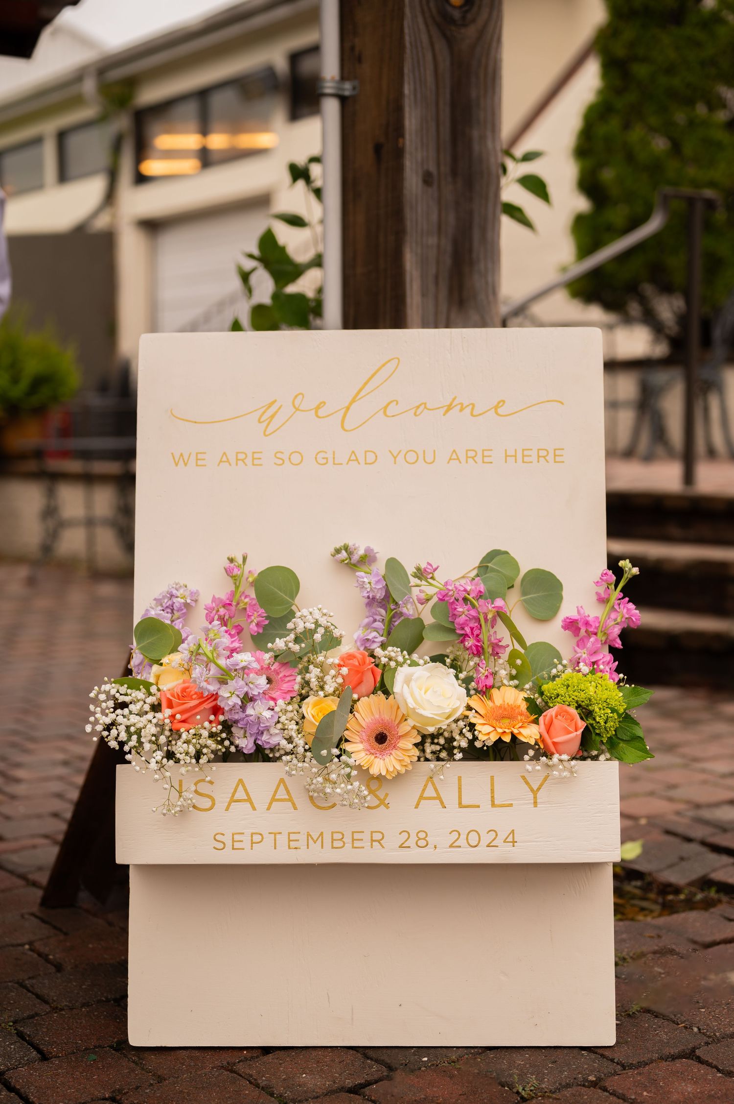 A trendy wedding welcome sign filled with colorful flowers and greenery on a white board. Wedding welcome floral holder.