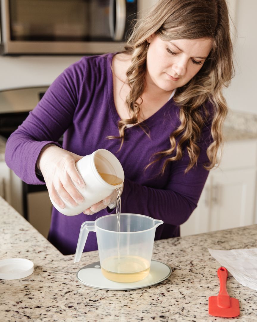 Someone in a purple sweater pouring liquid ingredients into a measuring cup on a granite countertop.