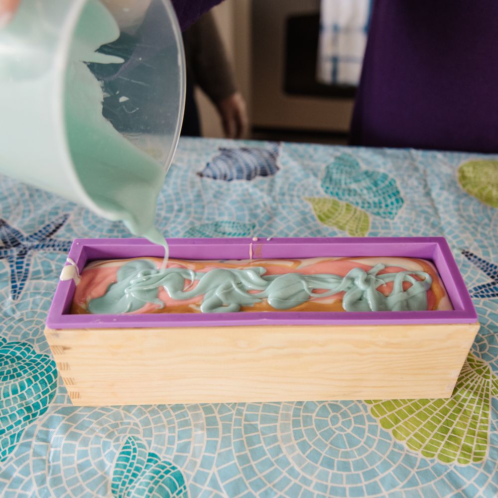 Pouring light colored liquid into a rectangular wooden mold with pink edges.