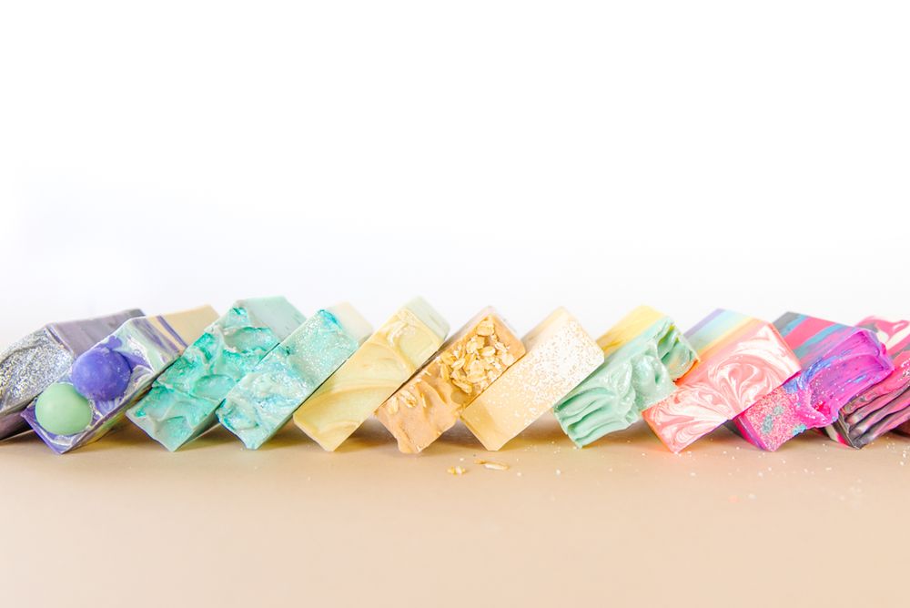 Colorful handmade soap bars arranged in gradient pattern against white background.