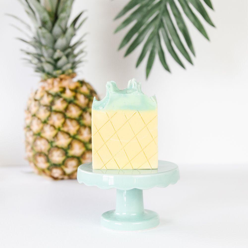 Pineapple themed cake on mint green cake stand with tropical palm leaf decor.