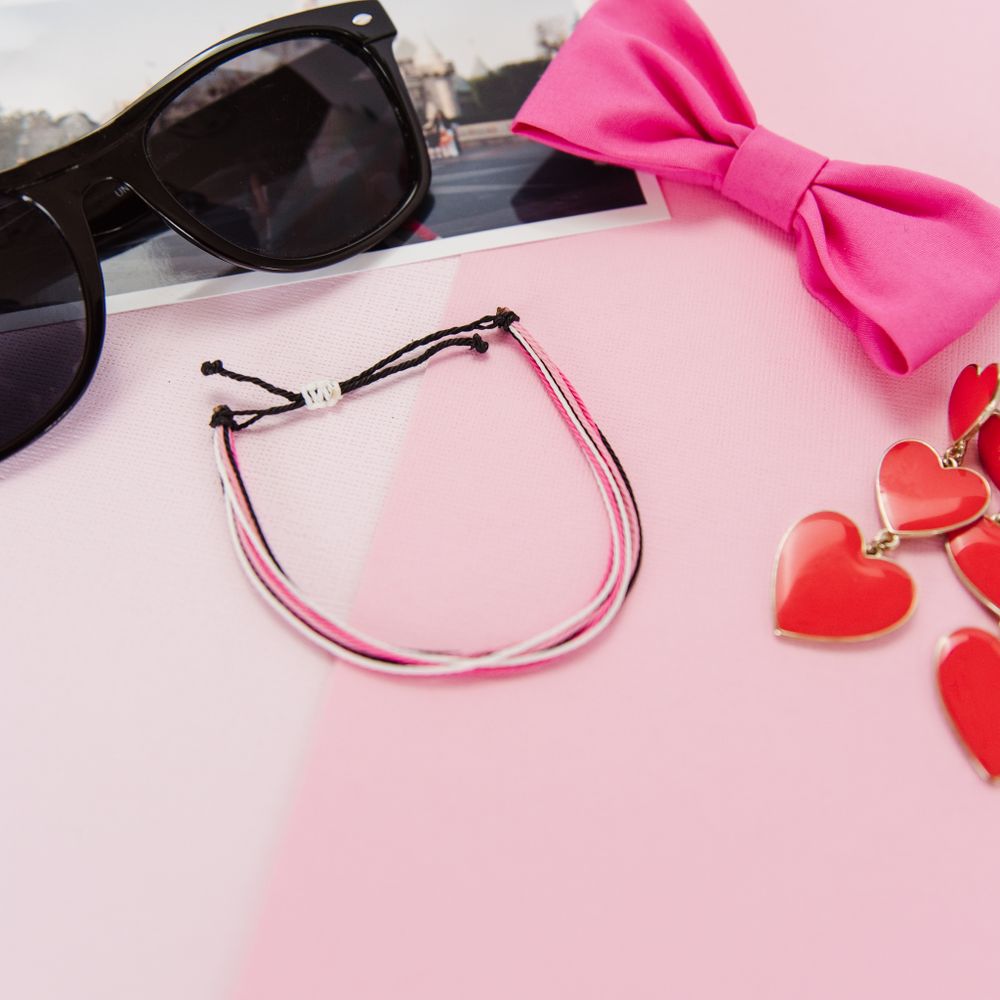 Pink headband with sunglasses, bow and heart decorations on pink and white background.