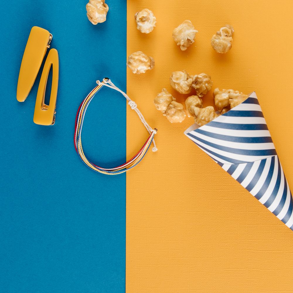 Popcorn spilling from striped party hat on blue and orange split background with hair accessories.