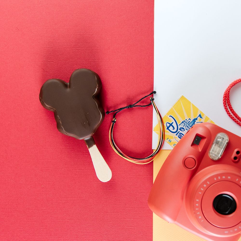 Mickey Mouse shaped chocolate ice cream bar keychain next to a red instant camera.