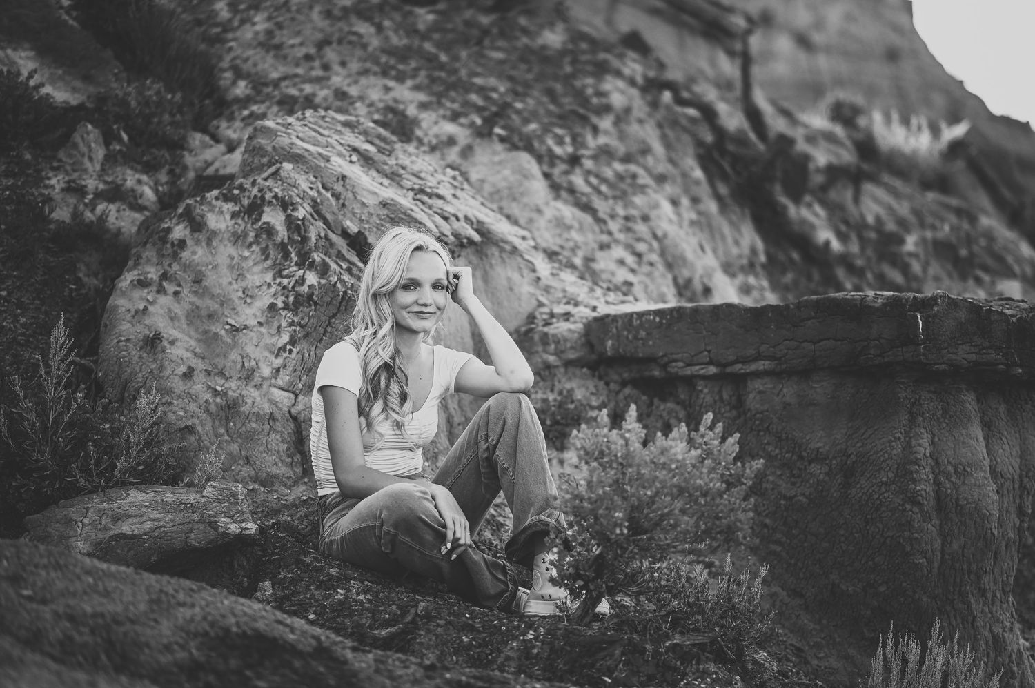 Black and white photo showing someone sitting on a rocky hillside against a weathered stone backdrop in natural lighting.