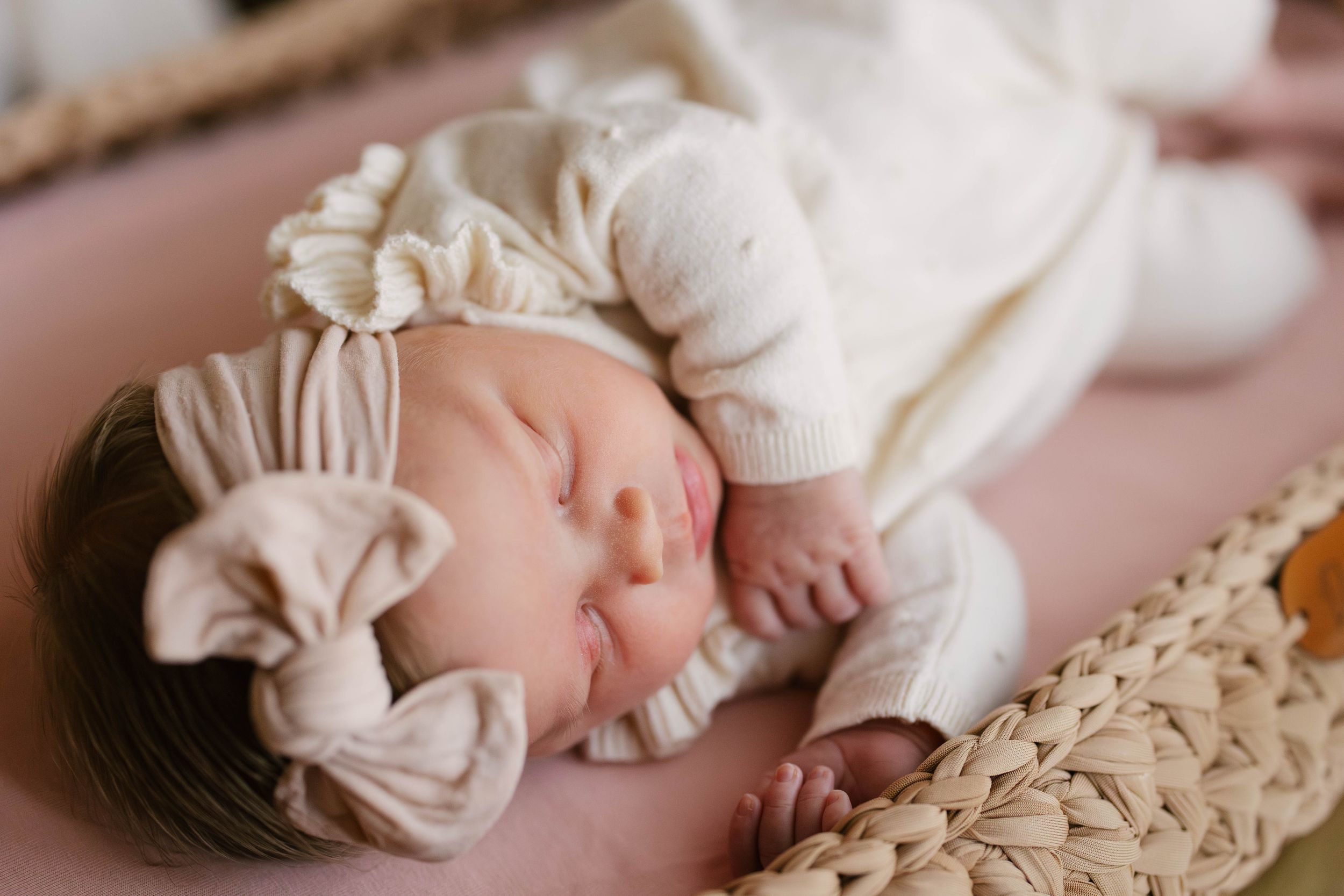 Sleeping newborn baby wrapped in white fabric lying on textured beige blanket in soft natural light.