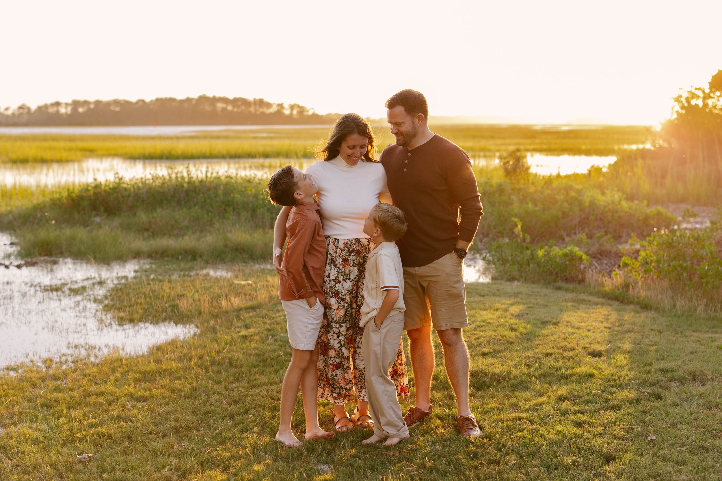 A family stands together on grassy marsh at sunset with golden light illuminating the coastal landscape.