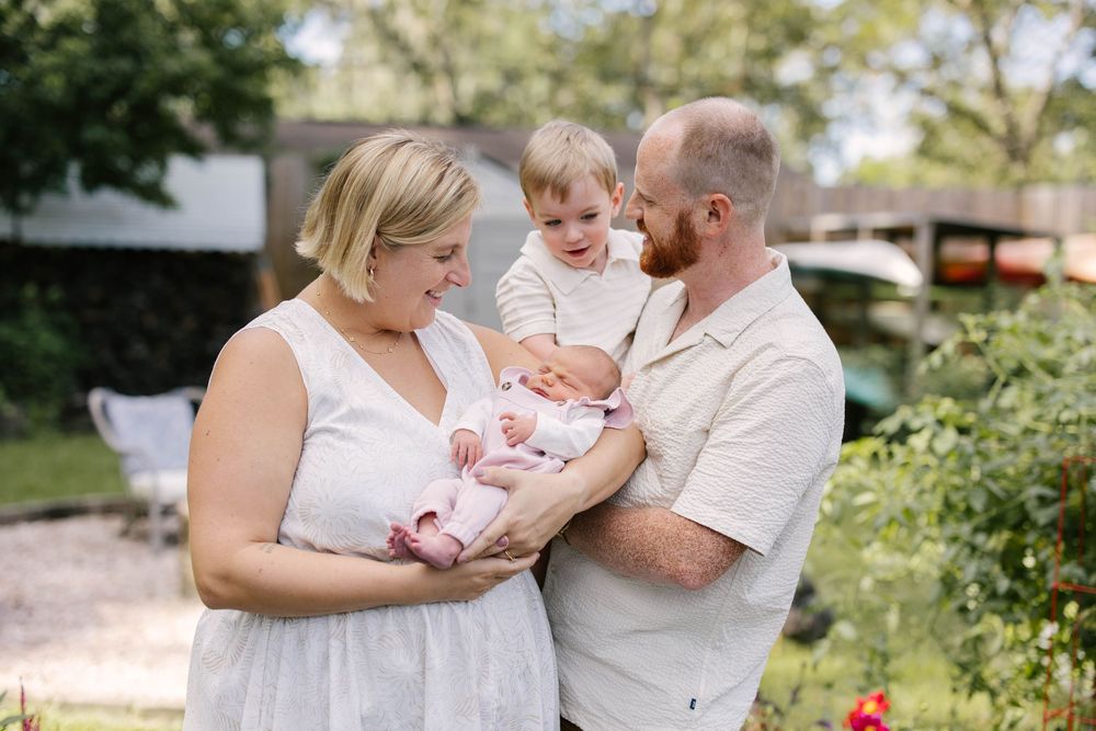 Family members share tender moments together with a baby in an outdoor garden setting.
