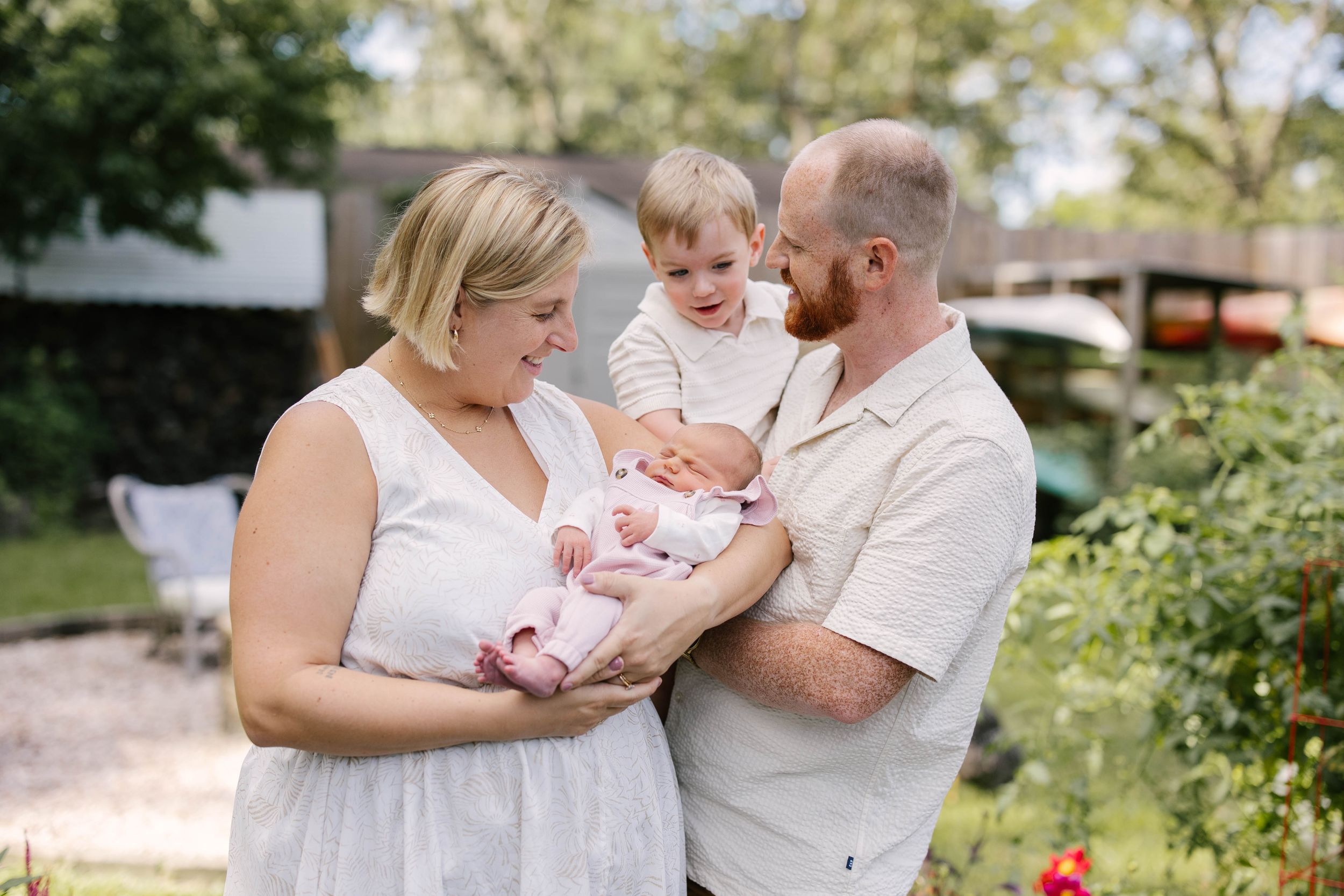 Family members share tender moments together with a baby in an outdoor garden setting.
