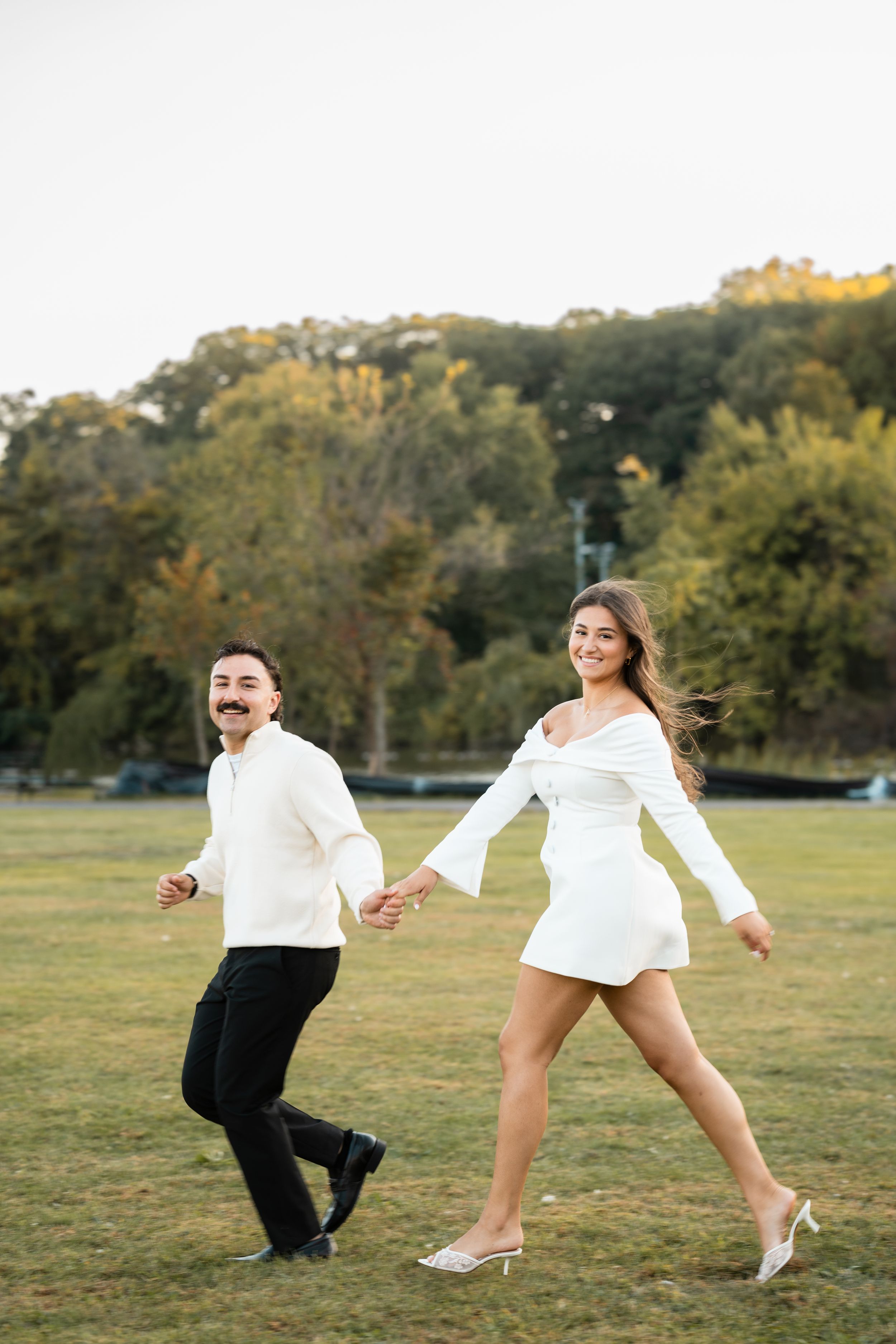 Playful couple jumping and dancing in a grassy field during a photo session.