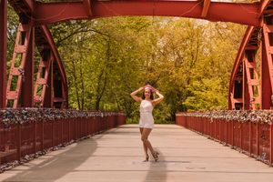 Girl in white dress in the middle of red bridge, wearing a pink graduation cap