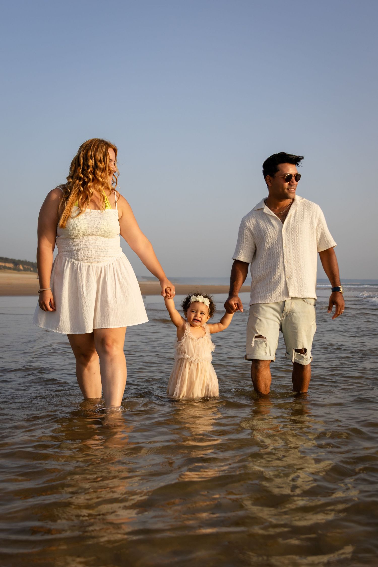 Family wading in shallow ocean water wearing coordinated white outfits.