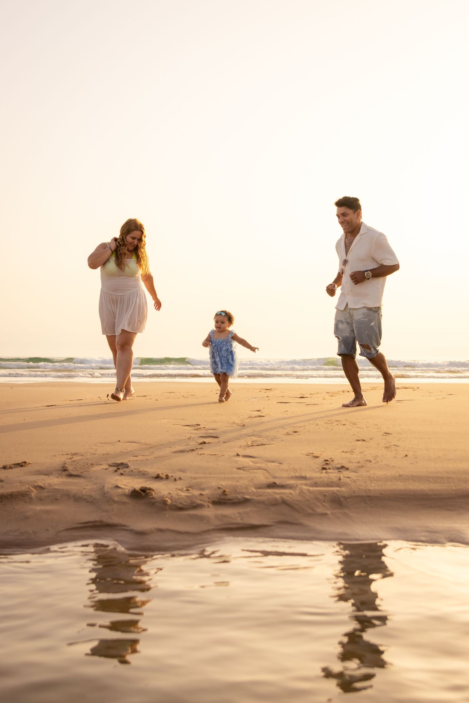 Family playing and running along the beach shoreline at golden hour.