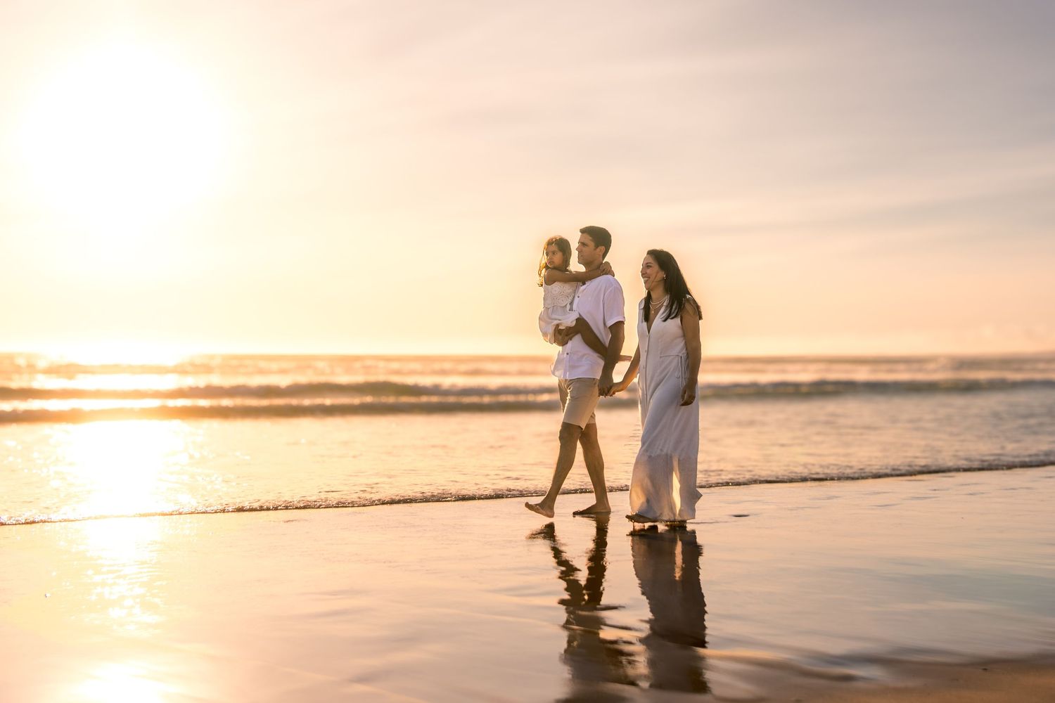 Silhouetted figures walking along beach shoreline during golden hour.