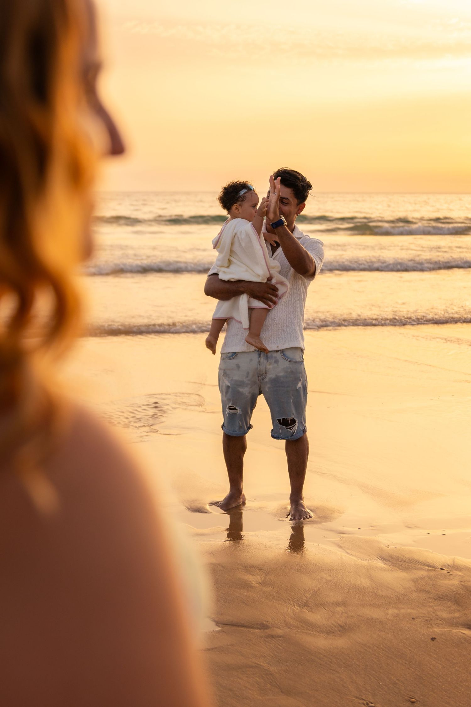 Couple walking hand in hand along the beach at sunset with orange sky in background.