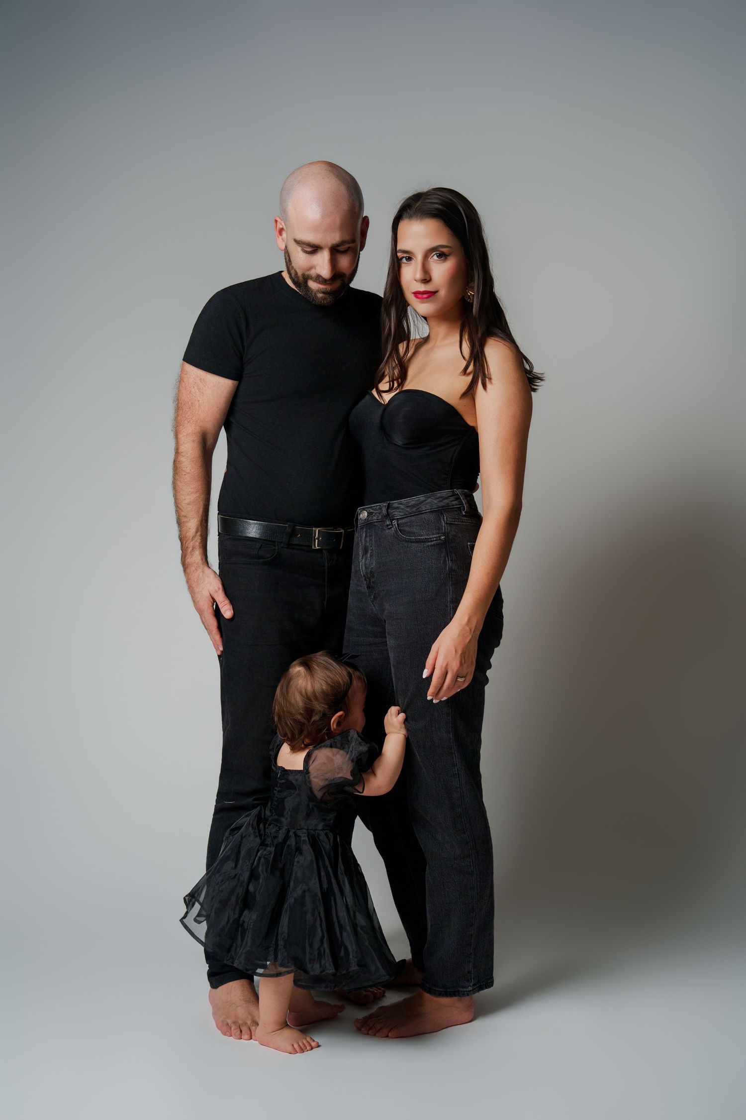 Family in black clothing poses together on grey studio backdrop.