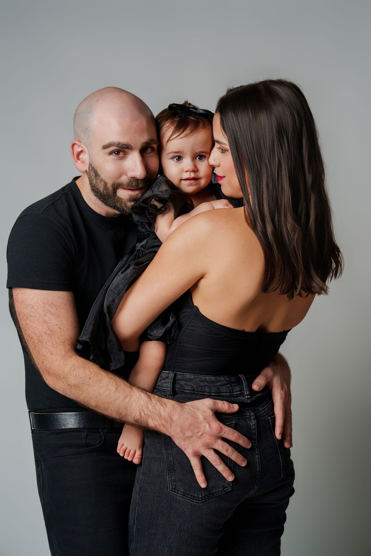 Family wearing black clothes embraces in intimate portrait series against gray background.