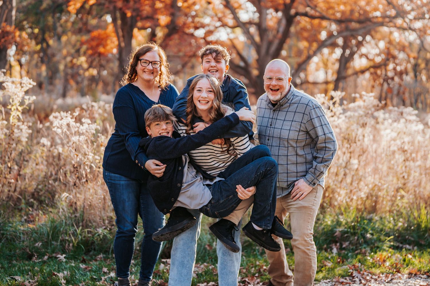 A loving family sharing a tender moment together outdoors during golden hour in tall grass and wildflowers.