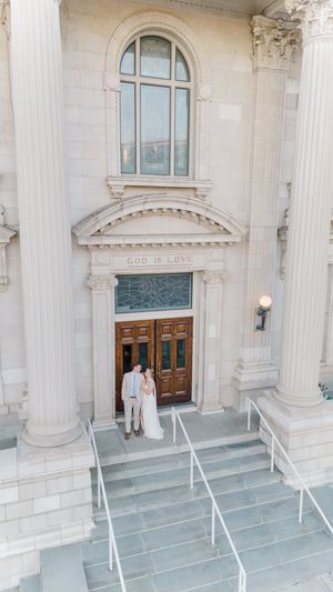 Bride and groom standing at entrance of classical stone church with God Is Love inscription.